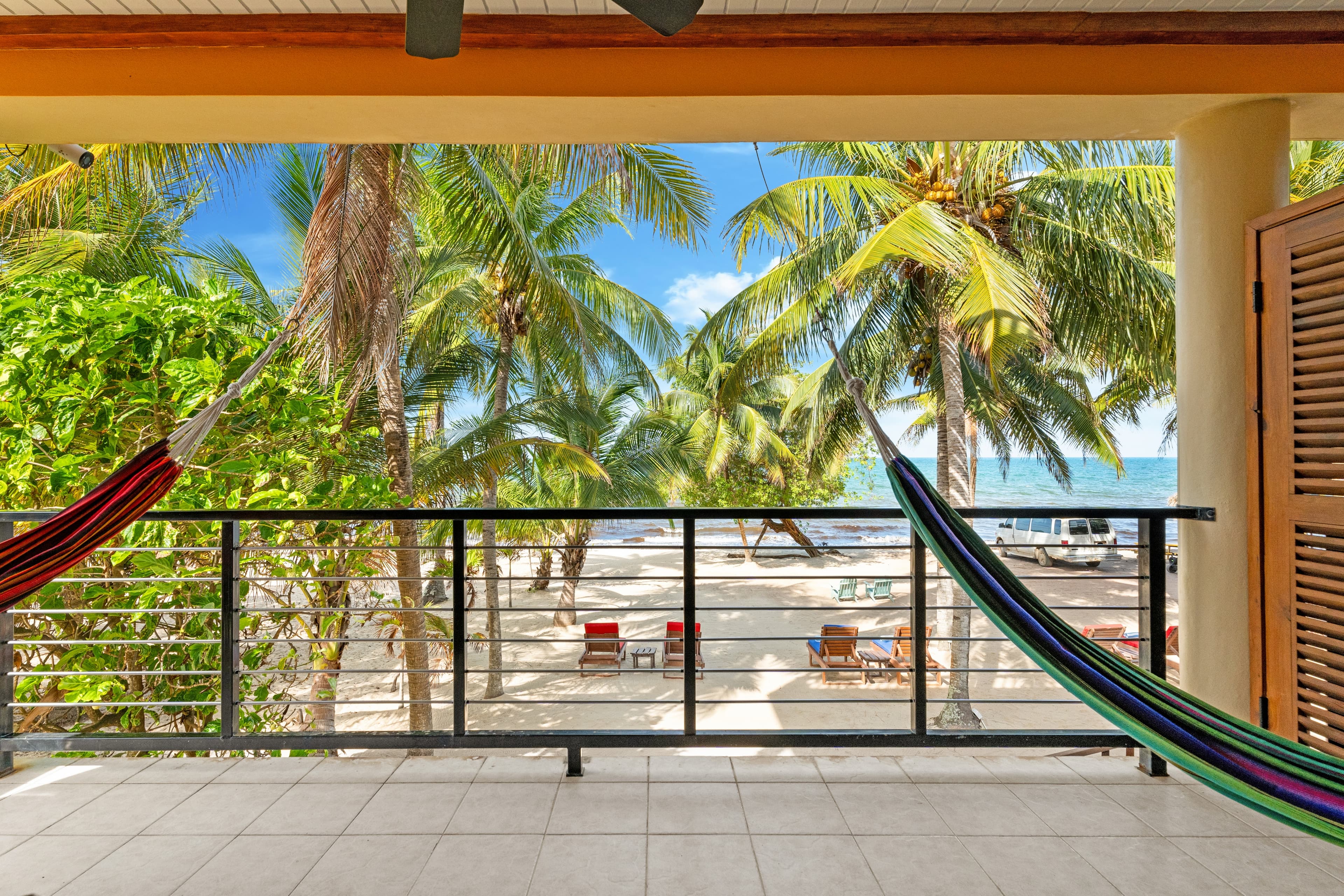 A balcony view featuring hammocks and palm trees overlooking a sandy beach and ocean.