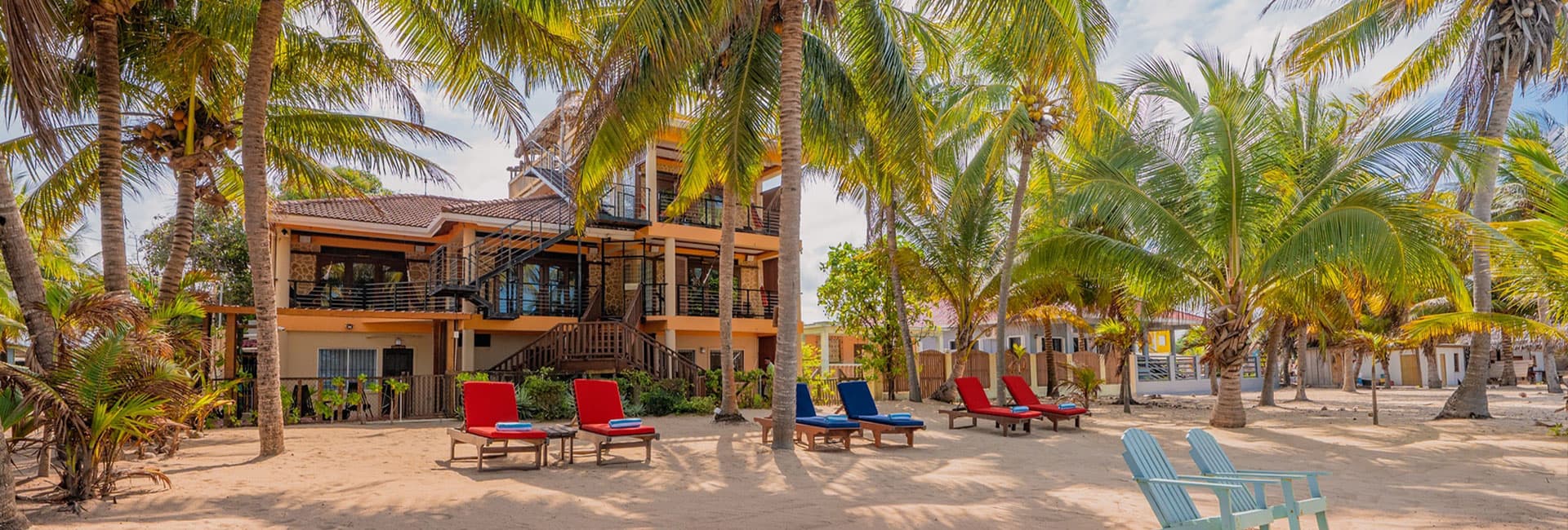 A beachfront property surrounded by palm trees and lounge chairs on the sand.