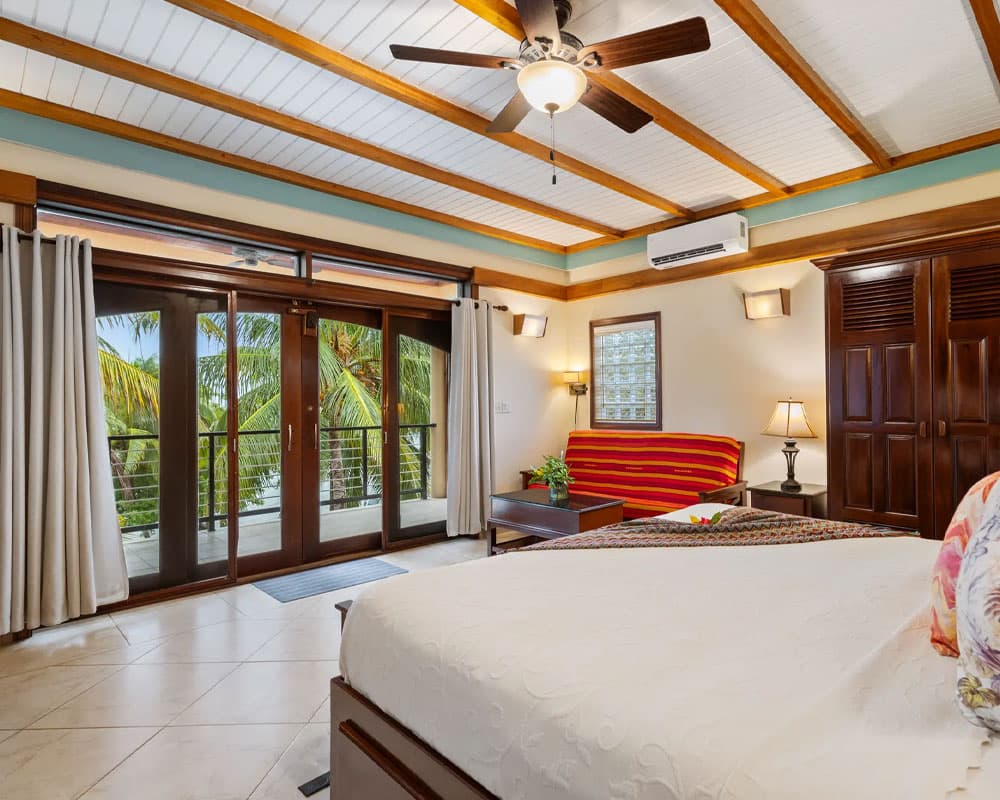 A bright, tropical-themed bedroom with a ceiling fan, large windows, and access to a balcony.